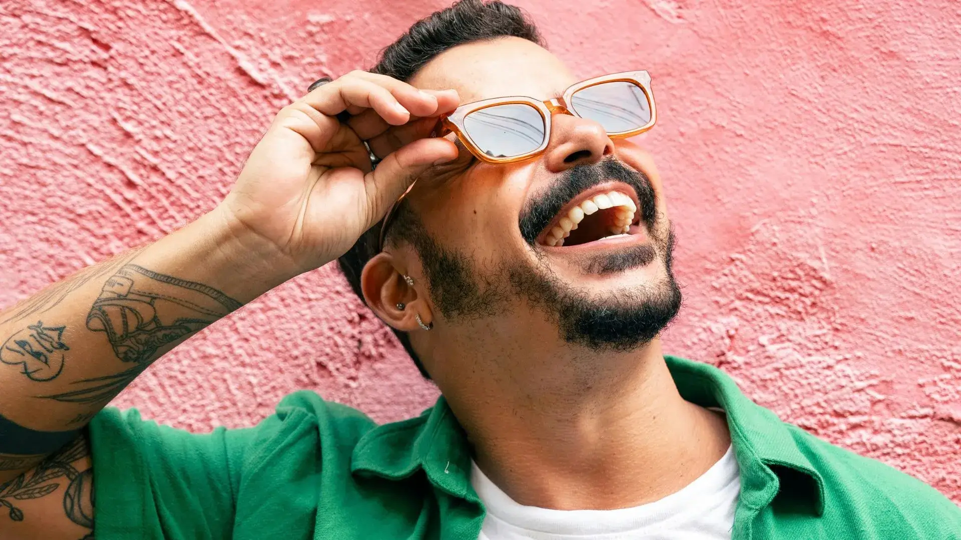 Homem sorridente usando óculos de sol e camisa verde, representando a felicidade e o impacto positivo do salário emocional no bem-estar dos colaboradores