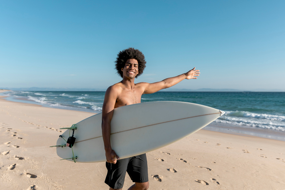 Homem segurando uma prancha de surf e apontando para o mar