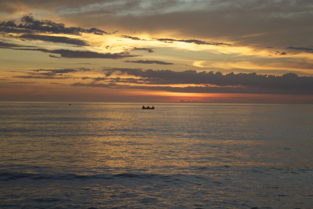 entardecer em arraial do cabo com barco de pescadores no horizonte e céu alaranjado na praia grande.