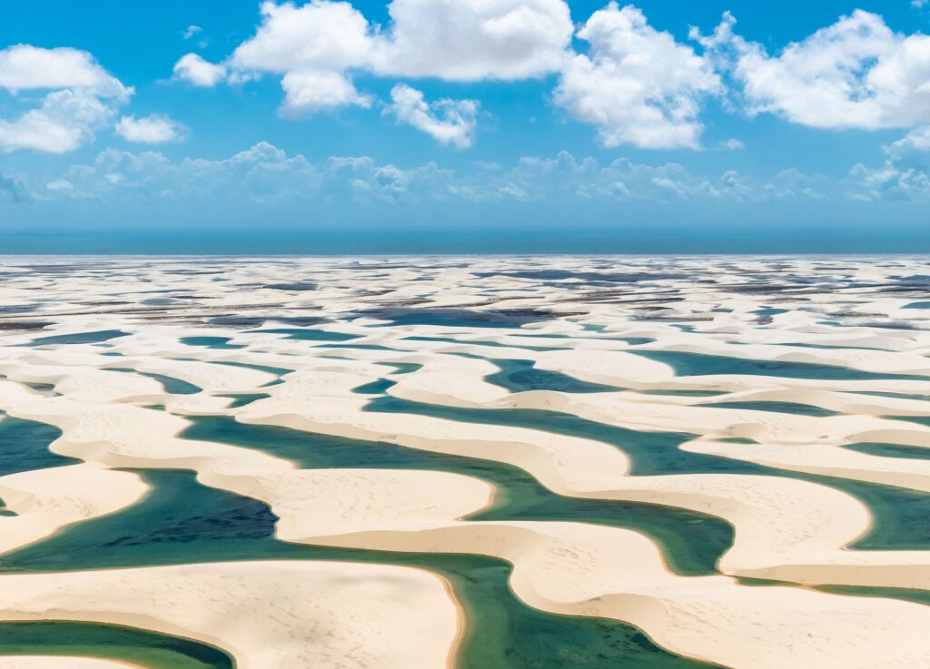 vista aérea dos lençóis maranhenses em julho com dunas brancas e lagoas de água turquesa até o horizonte.