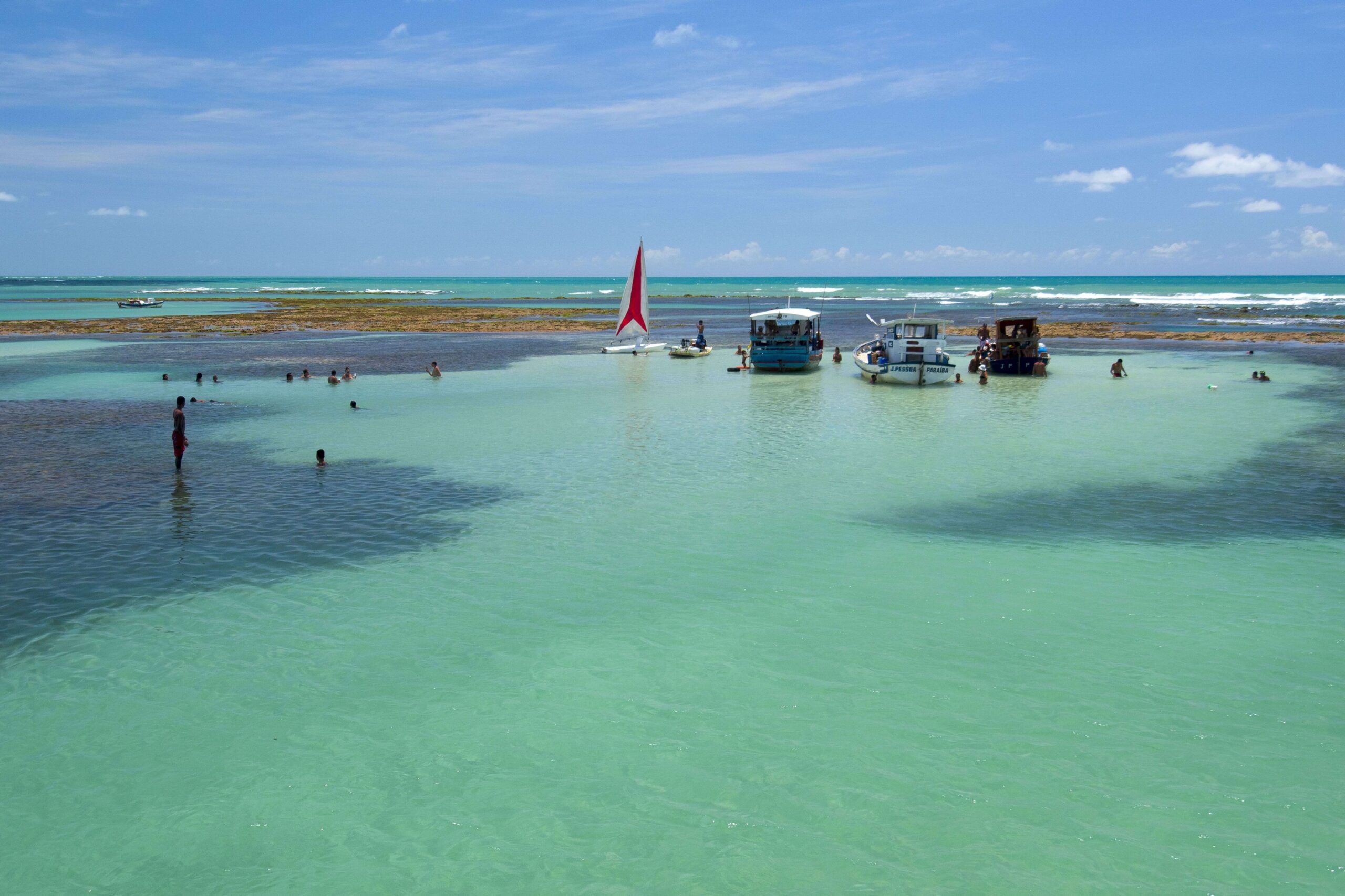 turistas nas piscinas naturais de joão pessoa com jangada e barcos ancorados em águas turquesa.