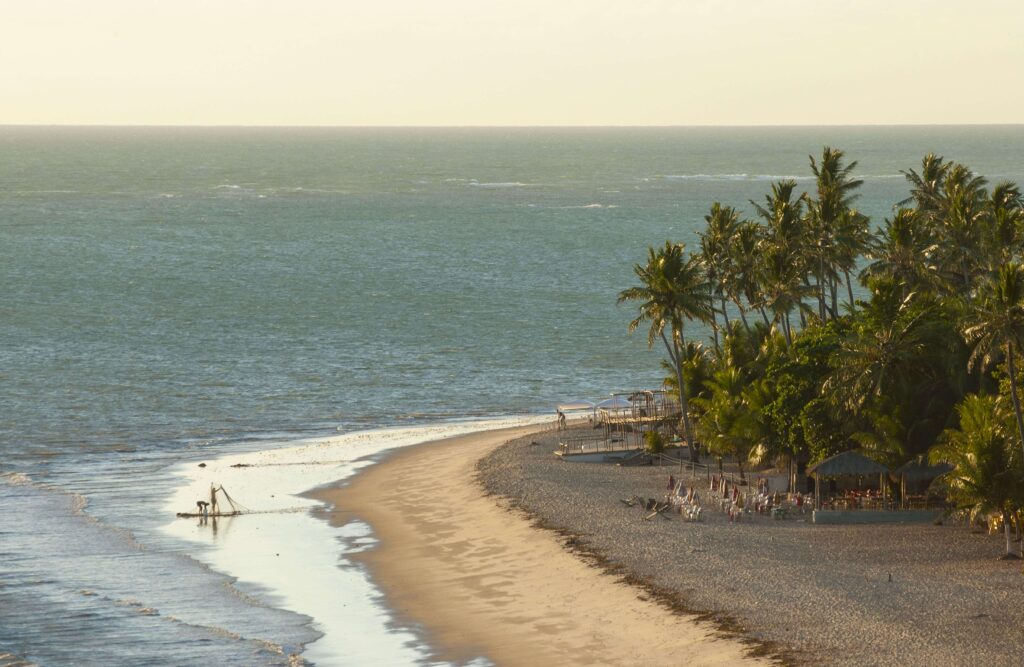 praia do seixas em joão pessoa com jangada de pescadores na areia, coqueiros e barracas ao entardecer.